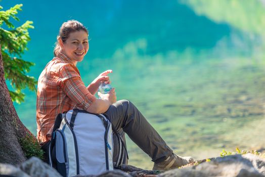 happy tourist with a bottle of water admires the beautiful mountain lake in the Tatras