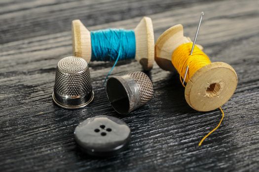 Thread with a thimble and button on black wooden background