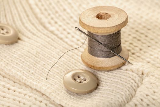 spool of thread with a needle on white knitted clothes