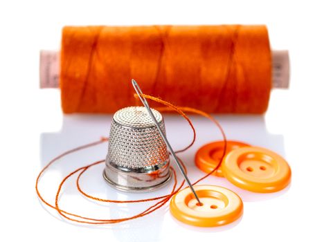 Needle with orange thread and buttons on a white background