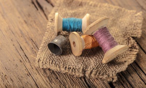 colored threads and thimble on wooden background