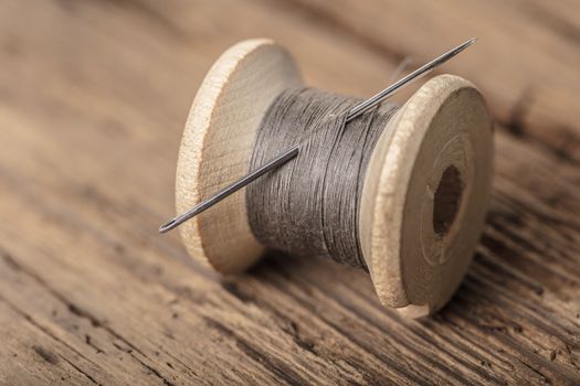 spool of thread with a needle on wooden background