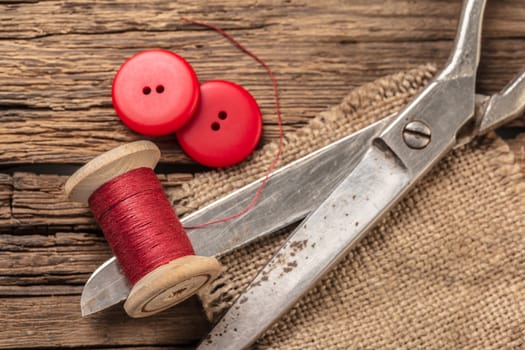 red thread with buttons and scissors, wooden background