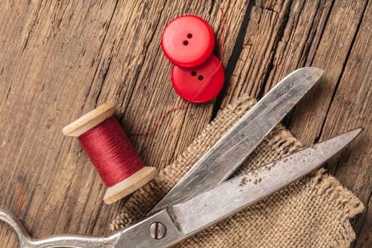 red thread with buttons and scissors, wooden background