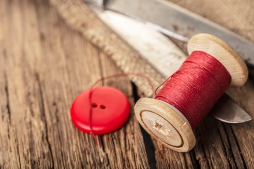 red thread with buttons and scissors, wooden background