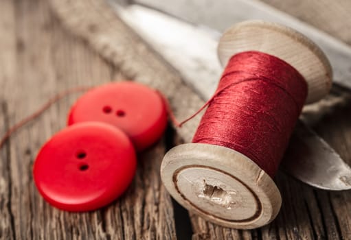 red thread with buttons and scissors, wooden background