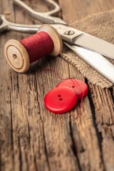 red thread with buttons and scissors, wooden background