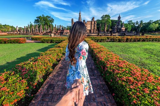 Woman holding man's hand and leading him to Wat Mahathat Temple in the precinct of Sukhothai Historical Park, Wat Mahathat Temple is UNESCO World Heritage Site, Thailand.