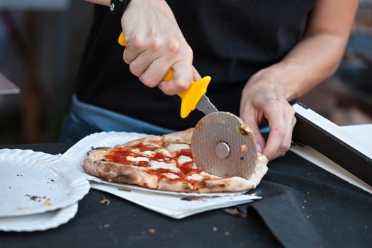 Pizza maker cutting a pizza margherita in slices ready to takeaway