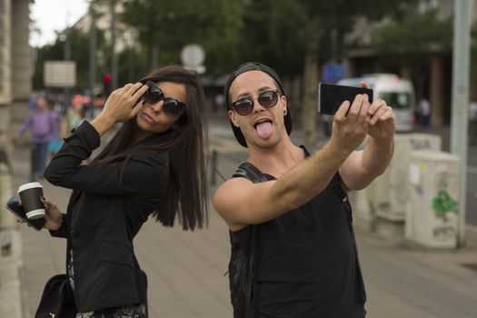 Young cheerful friends taking photos of themselves on smart phone, urban city outdoor scene, selective focus