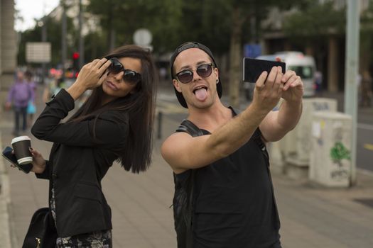 Two cheerful friends taking photos of themselves on smart phone, urban city outdoor scene, selective focus