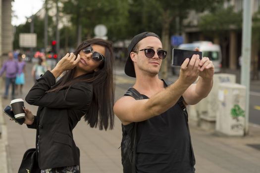 Cheerful friends taking photos of themselves on smart phone, urban city outdoor scene, selective focus