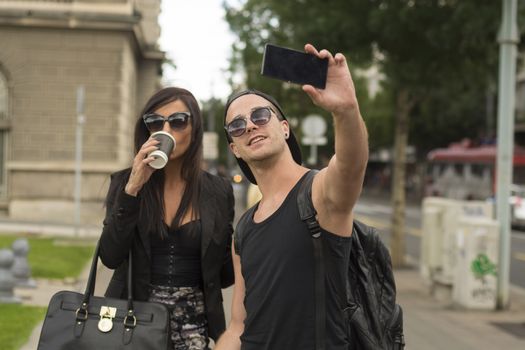 Two cheerful friends taking photos of themselves on smart phone, urban city outdoor scene, selective focus