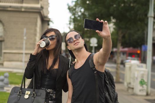 Cheerful friends taking photos of themselves on smart phone, urban city outdoor scene, selective focus