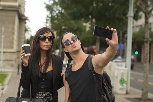 Two cheerful friends taking photos of themselves on smart phone, urban city outdoor scene, selective focus