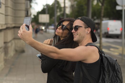 Young cheerful friends taking photos of themselves on smart phone, urban city outdoor scene, selective focus