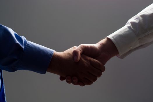 Low angle view of two businessmen hands shaking over dark gray background and light source at bottom side