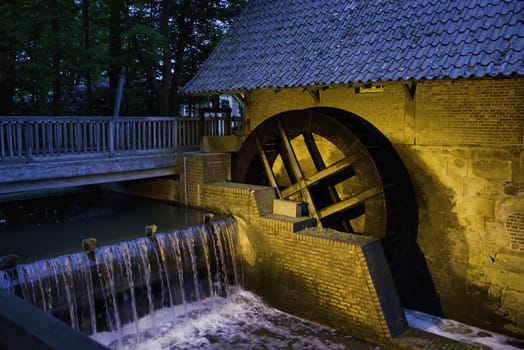 Small river with historic paddle wheel in Haarmuhle, Germany, Europe, this one is still working and more then 400 years old in the evening with lights