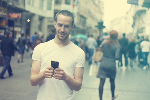 Smiling Man with mobile phone walking, background is blured city