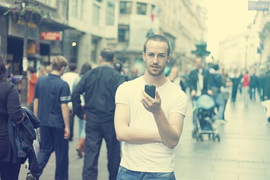 Young Man in city with mobile phone walking, background is blured city street