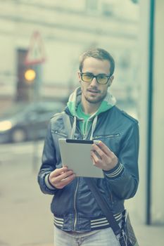 Young man with yellow glasses use iPad tablet computer on street, public space. Blurred background