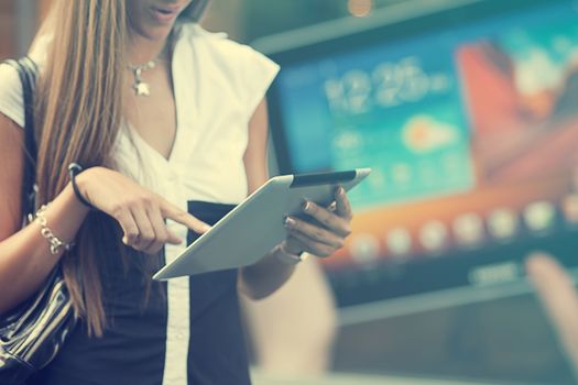 Young Woman with tablet computer walking on street, downtown. In background is blured advertisiment with OpenSource graphics. Visible noise