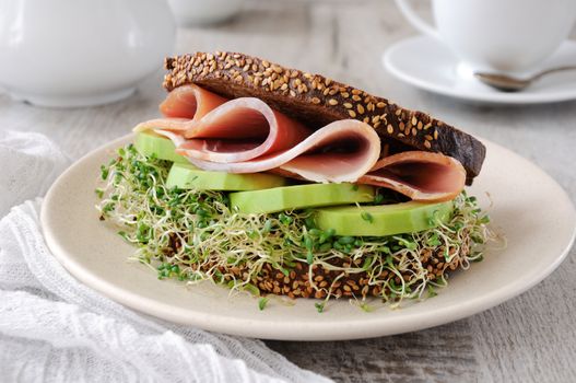  Sandwich of rye bread with cereals, slices of ham and avocado with sprouts of sprouted alfalfa.