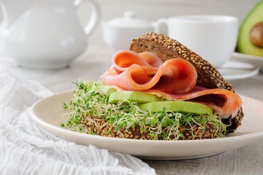 Sandwich of rye bread with cereals, slices of ham and avocado with sprouts of sprouted alfalfa.