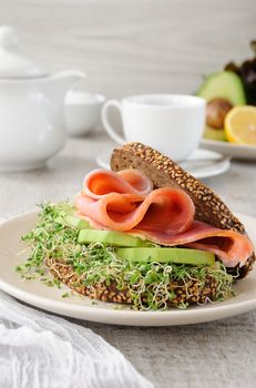 Sandwich of rye bread with cereals, slices of ham and avocado with sprouts of sprouted alfalfa.