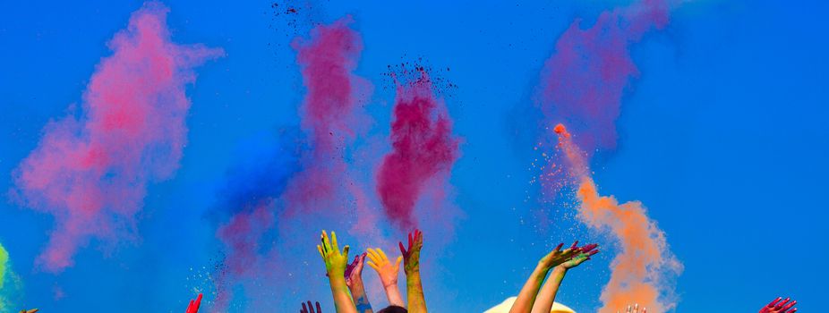 At the color Holi festival, hands in the air, blue sky behind