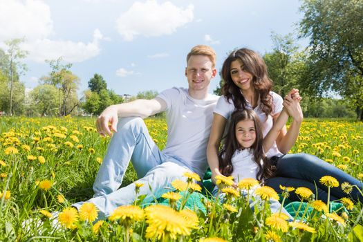 Portrait of happy family sitting on flower field in park on a sunny day