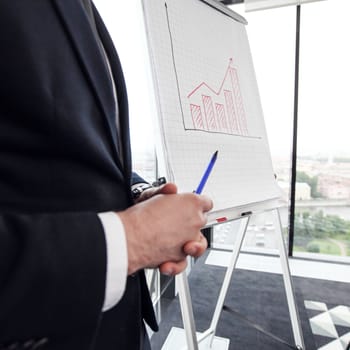 Business man standing near flipchart at presentation in office analyzing financial graph