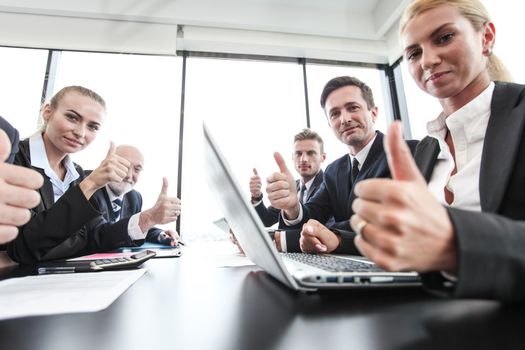 Mixed group of people in business meeting working with documents and computers showing thumbs up