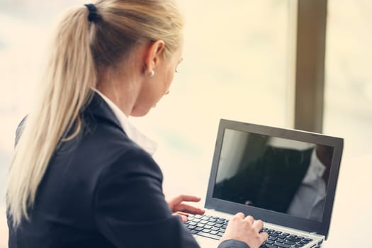 Business woman typing on laptop sitting by the window in office