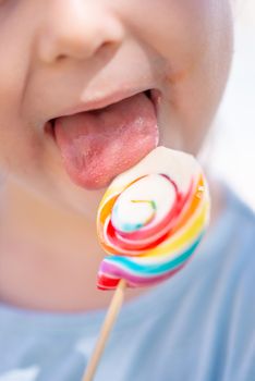 Little kid, child with colorful lolipop, licking on the lolipop, unrecognizable