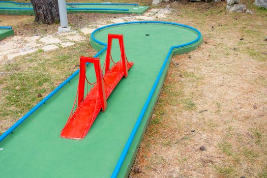 Mini golf course with obstacles, red suspension bridge