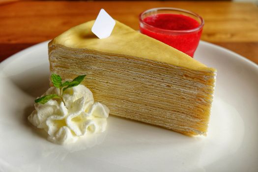 Crepe cake with cream and strawberry and sauce in ceramic cup on white plate.