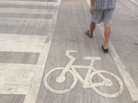 The man walking near  bicycle road sign on concrete floor.
