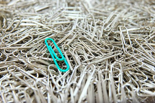 Green paper clip on multiple paper clips background.