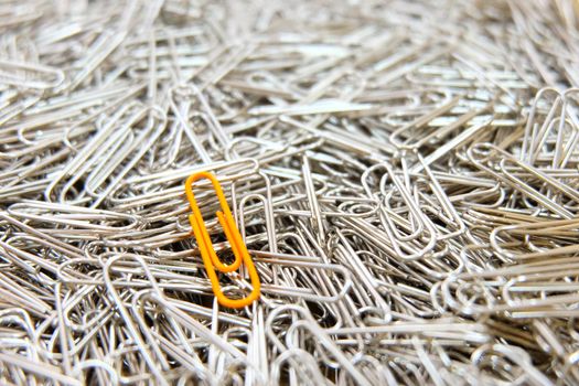 Orange paper clip on multiple paper clips background.