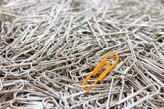 Orange paper clip on multiple paper clips background.