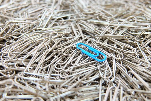 Blue paper clip on multiple paper clips background.