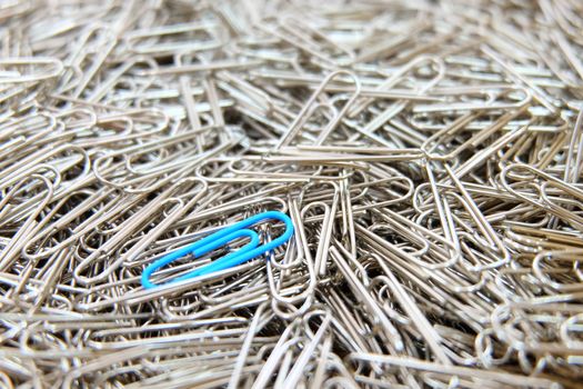 Blue paper clip on multiple paper clips background.
