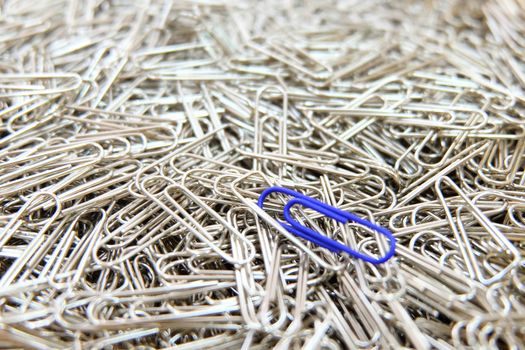 Dark blue paper clip on multiple paper clips background.