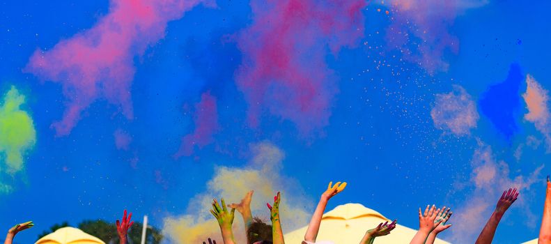 At the color Holi festival, hands in the air, blue sky behind
