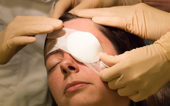 Doctor covering eye of female patient by medical plaster