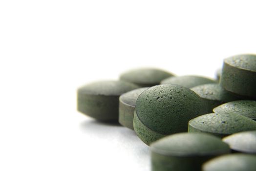 Close up of many organic spirulina tablets with low depth of field over white background. 