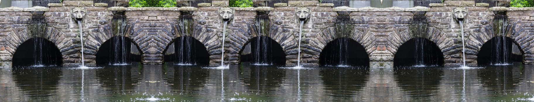 Fountain with waterfall with rock stone decoration in the garden or park. Landscape design detail.