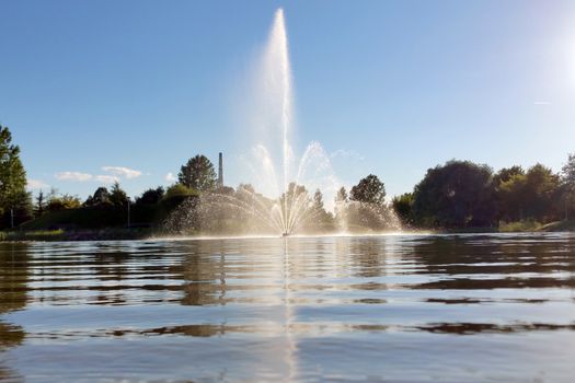 fountain on lake reflected in water, against blue sky background.