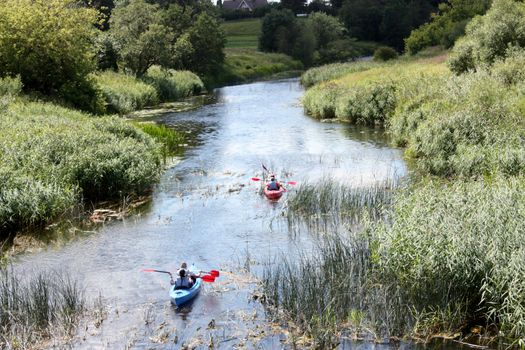 active rest on the river. People on kayaks are sailing along a plain small river. Picture taken from the back on a summer day